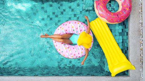 Frau entspannt sich auf aufblasbarem Donut im Pool daneben sind aufblasbarer Ring und Matratze