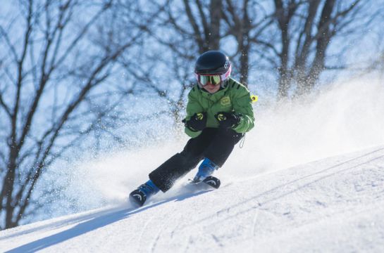 Winterbild Kind in grüner Jacke am Ski fahren