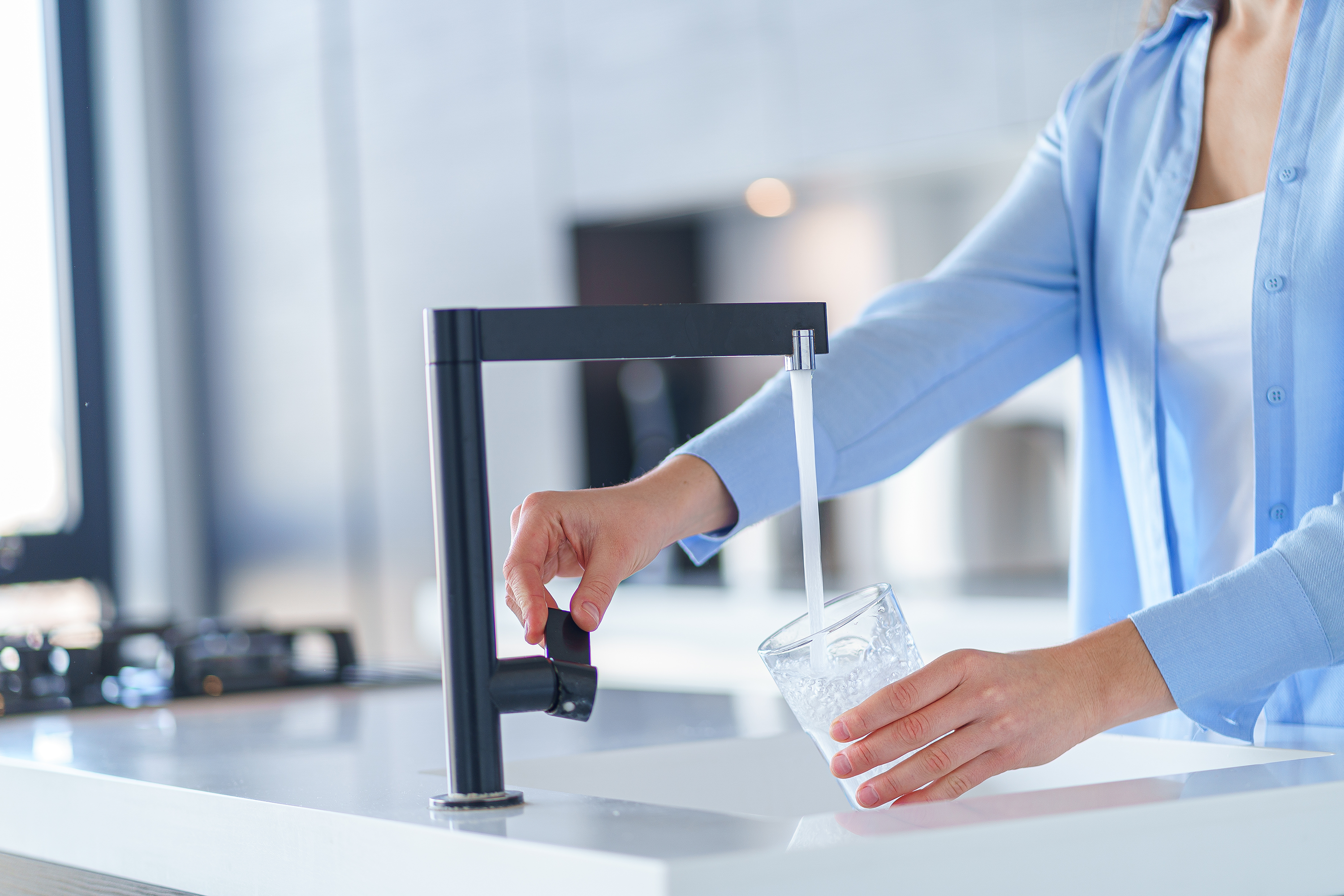 Frau im blauen Hemd füllt ein Glas mit Leitungswasser