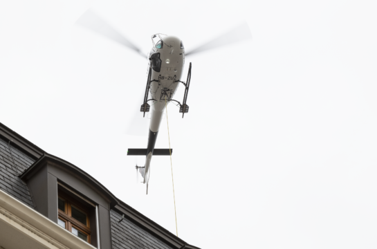 weisser Helikopter fliegt über einem Haus