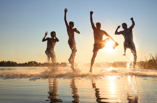 vier Männer springen bei Sonnenuntergang aus dem See